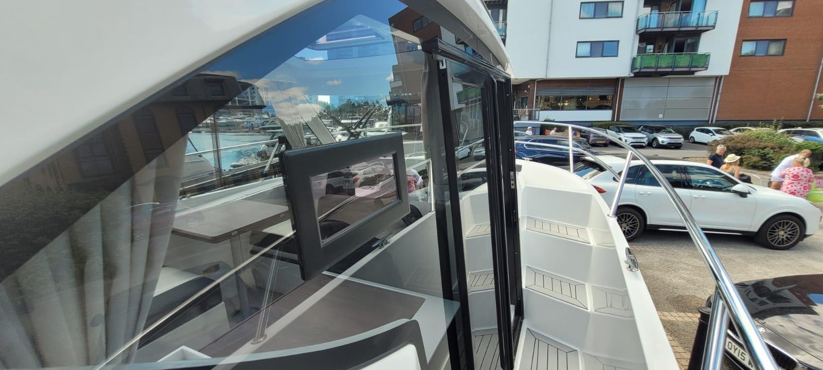 View of a modern boat interior with a boat window, seating area, and reflection of a marina visible outside.